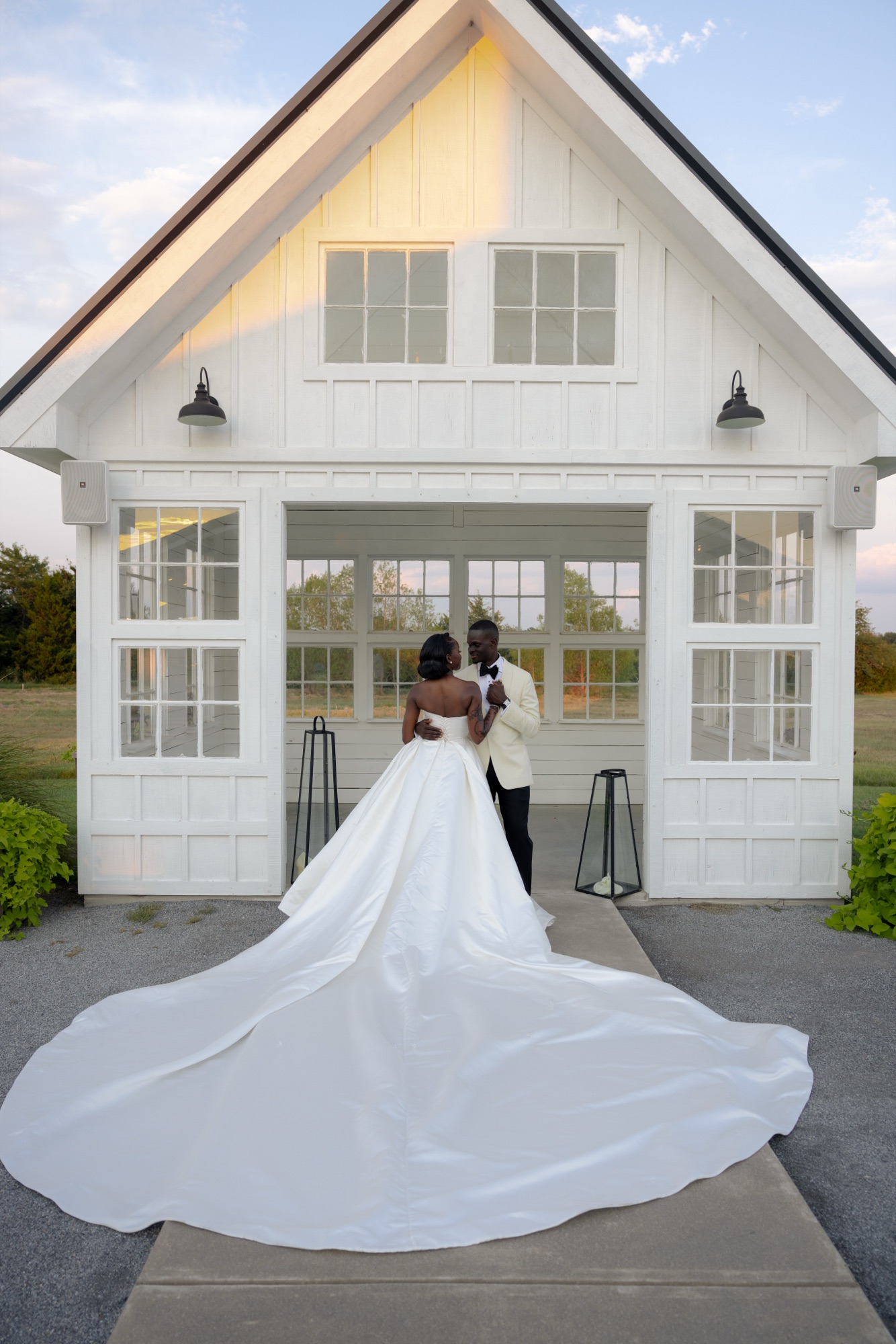 Bride and groom in front of a white barn, wedding gown with custom train and design additions, Dallas TX