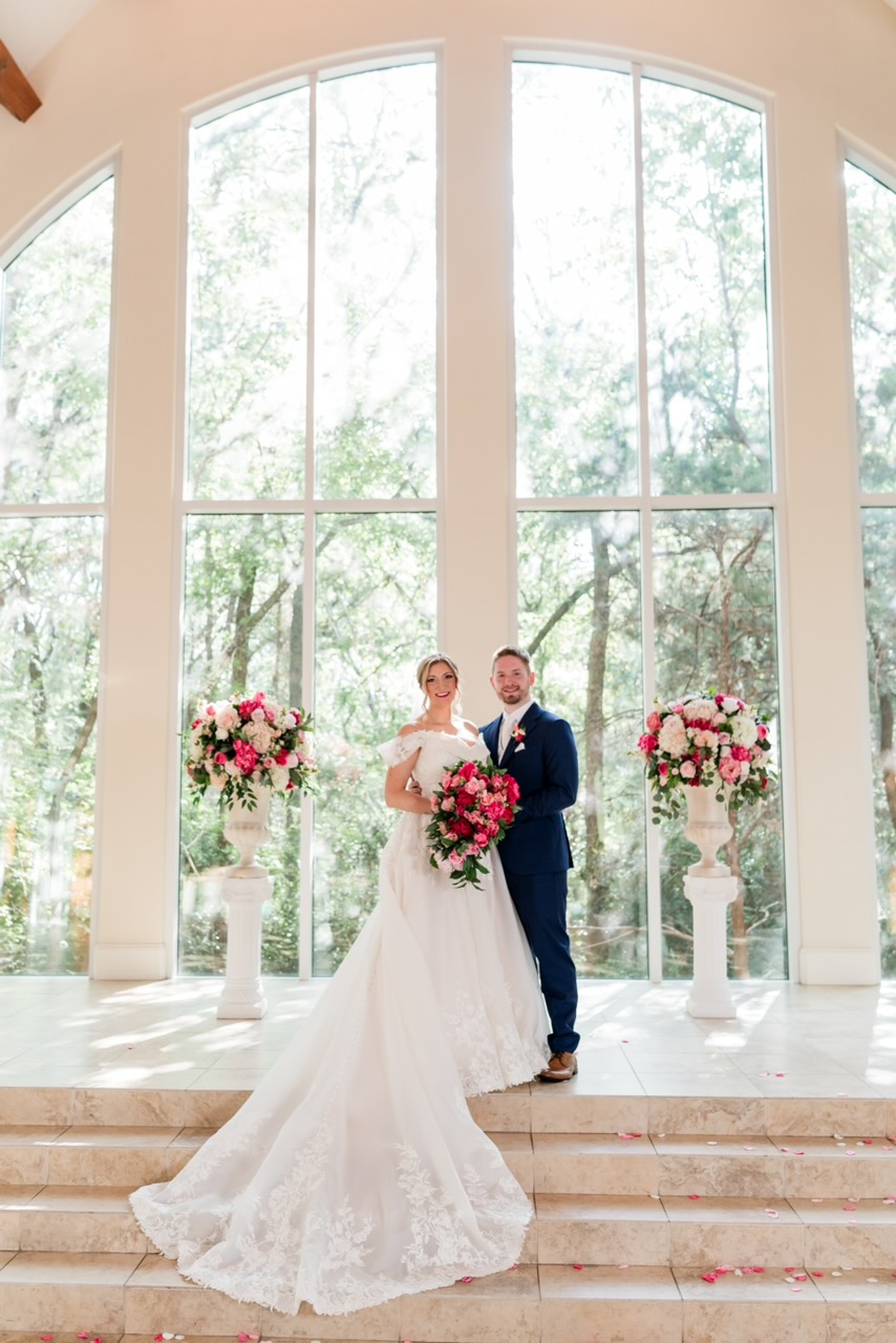 Bride and groom in a glass chapel with pink florals, lace wedding gown with train altered by Margo West Bridal Couture, Dallas TX
